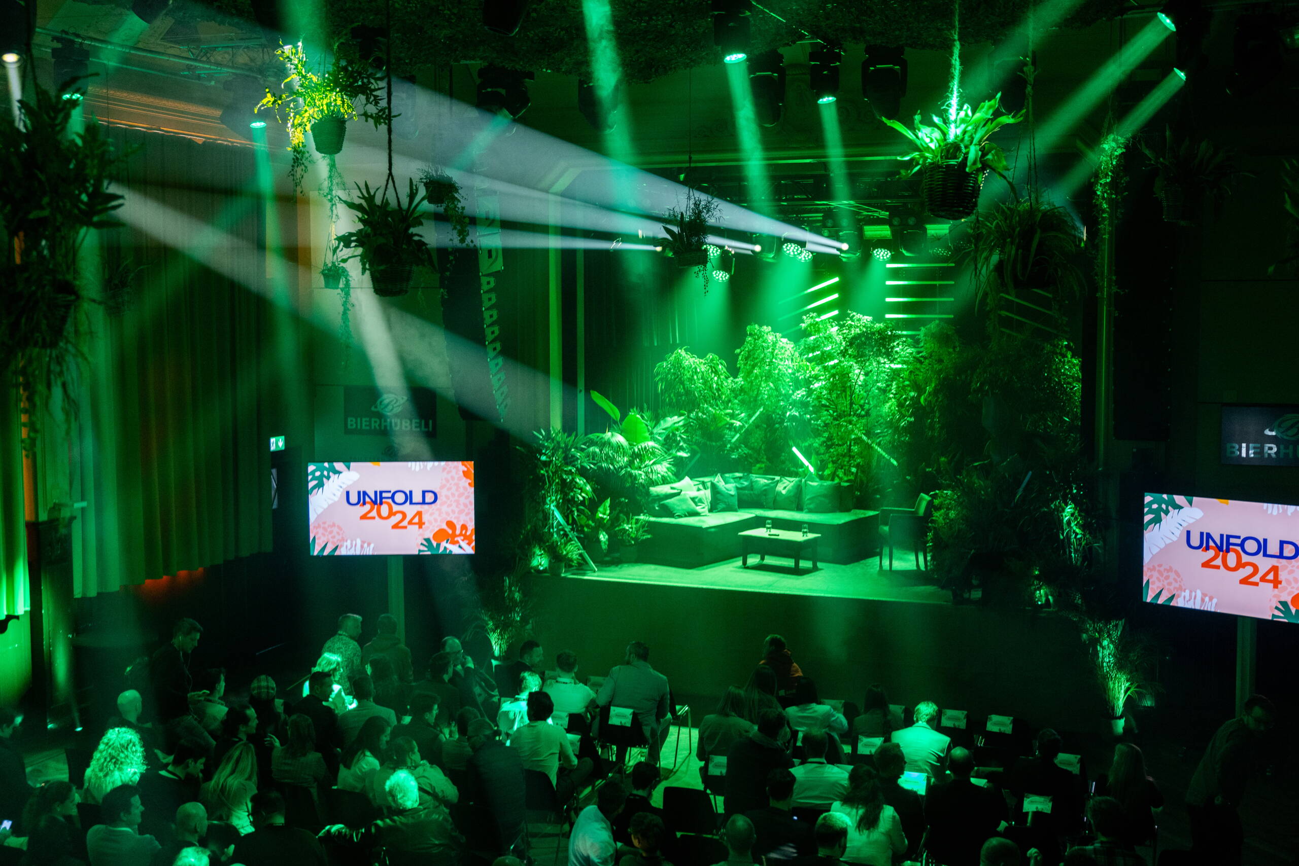 cleverclip_unfold2024.jpg Bühnenbild im Dschungel-Look mit grünem Licht und üppiger Bepflanzung beim Corporate Event Unfold 2024 von Cleverclip im Bierhübeli Bern. Corporate Event, Eventbühne, Eventdesign, Bierhübeli Bern, grüne Lichtstimmung, Dschungel Deko, Business Event, Eventagentur Schweiz, live kommunikation, Eventagentur bern, eventplanung, firmenevents, teamevents bern, jubiläumsfeier, networking anlass, mitarbeiter:innenanlass, Technik, Public Events, Sport und Entertainment Events, markenerlebnis, Brand Experience